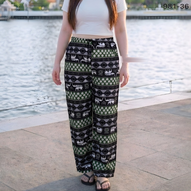 Woman wearing green and black elephant print wide-leg trousers by the water